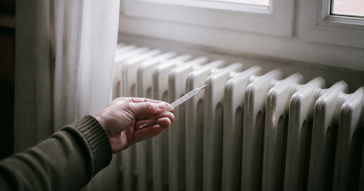 Main tenant un thermomètre devant radiateur froid immobile