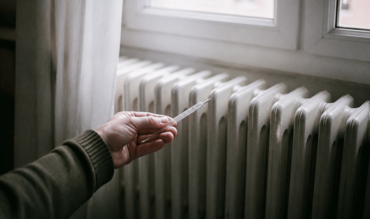 Main tenant un thermomètre devant radiateur froid immobile