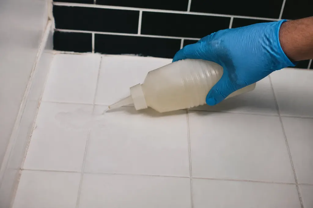 Main avec gant bleu appliquant liquide sur carreau blanc