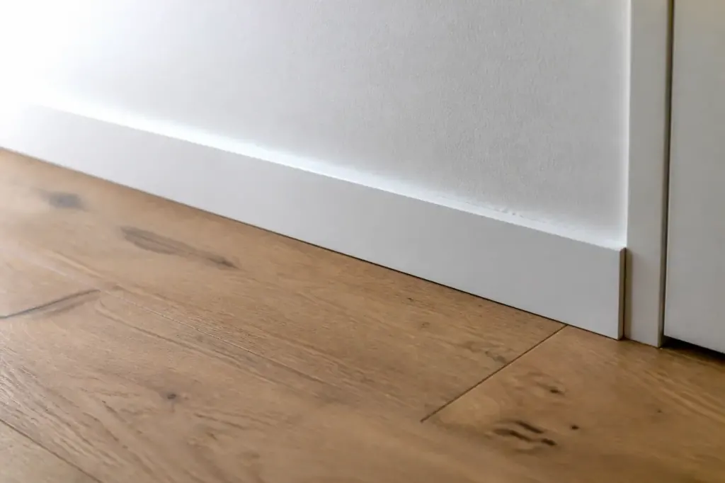 Plinthe blanche fixee au mur pres du parquet